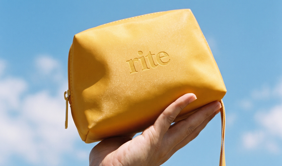 mão segurando uma bolsa necessaire amarela com o logotipo da marca rite cosmetics
